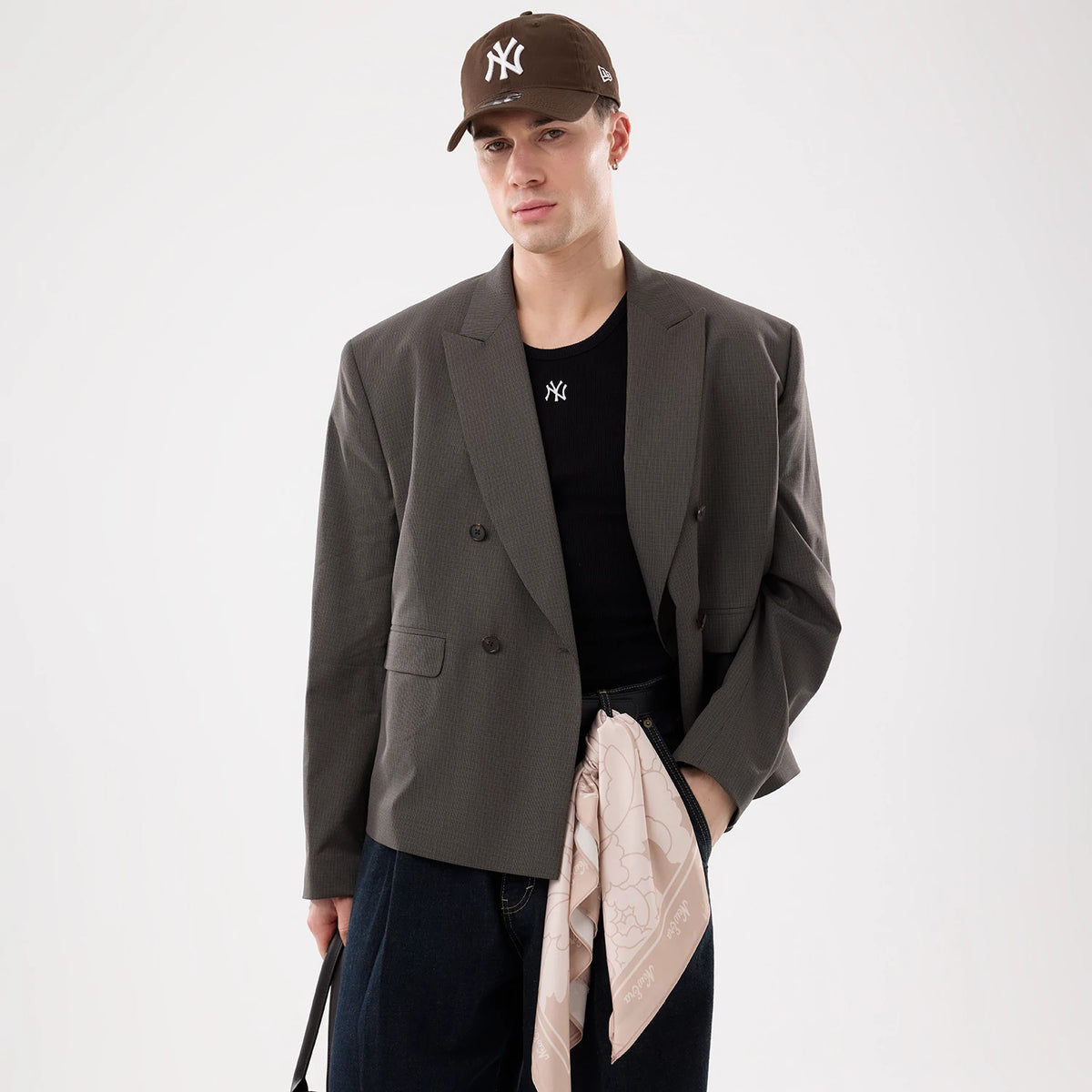 New Era Floral Satin Beige Bandana, on-model view with a solid black t-shirt and grey blazer, showing a floral pattern throughout the fabric, tied at the waist, and a border featuring the New Era logo.