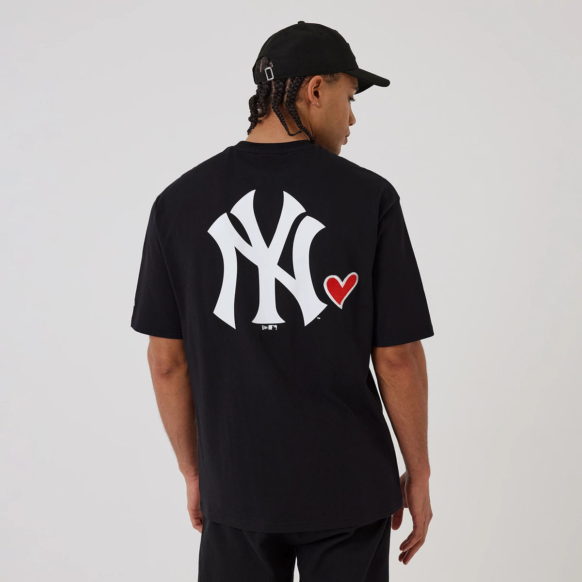 New Era New York Yankees MLB Heart Graphic Black T-Shirt, back view on a model with a black cap, featuring a large white embroidered Yankees logo paired with a red heart graphic on the right side, adding a design to the black shirt.