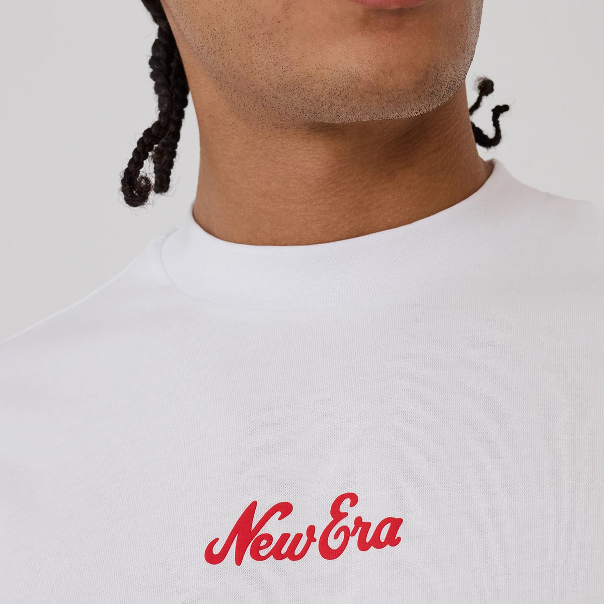 New Era Love Graphic White T-Shirt, front view on a model showing a white shirt with a red printed New Era logo on the chest below the collar, featuring a round neckline and a plain design across the fabric.