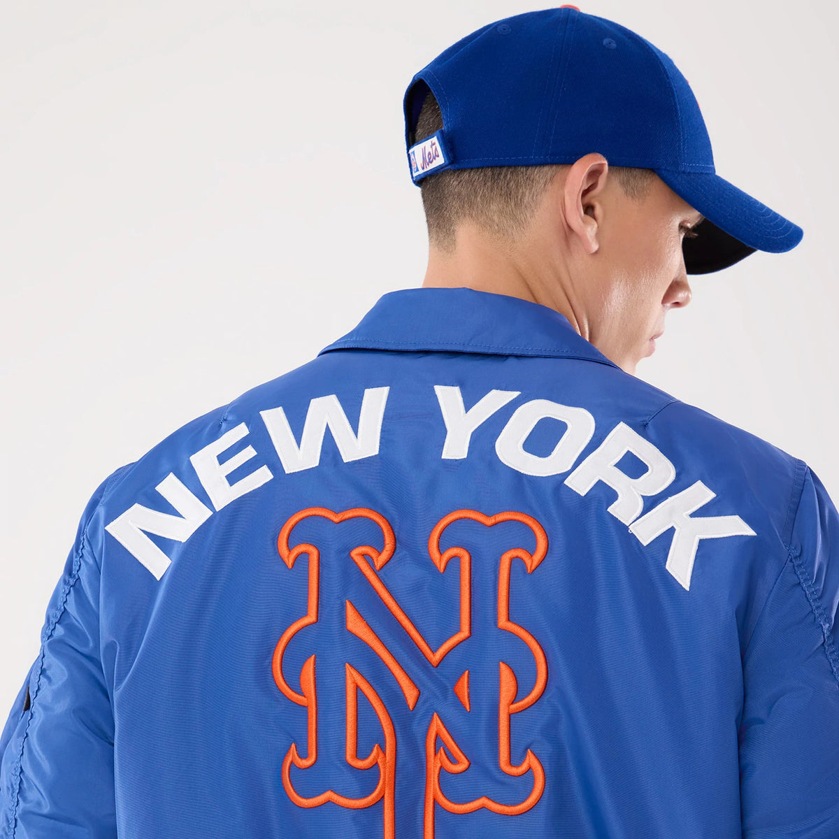 New Era New York Mets MLB X Alpha Blue Jacket, back view on-model showing large white embroidered NEW YORK lettering across the shoulders, an oversized orange-outlined Mets logo beneath.