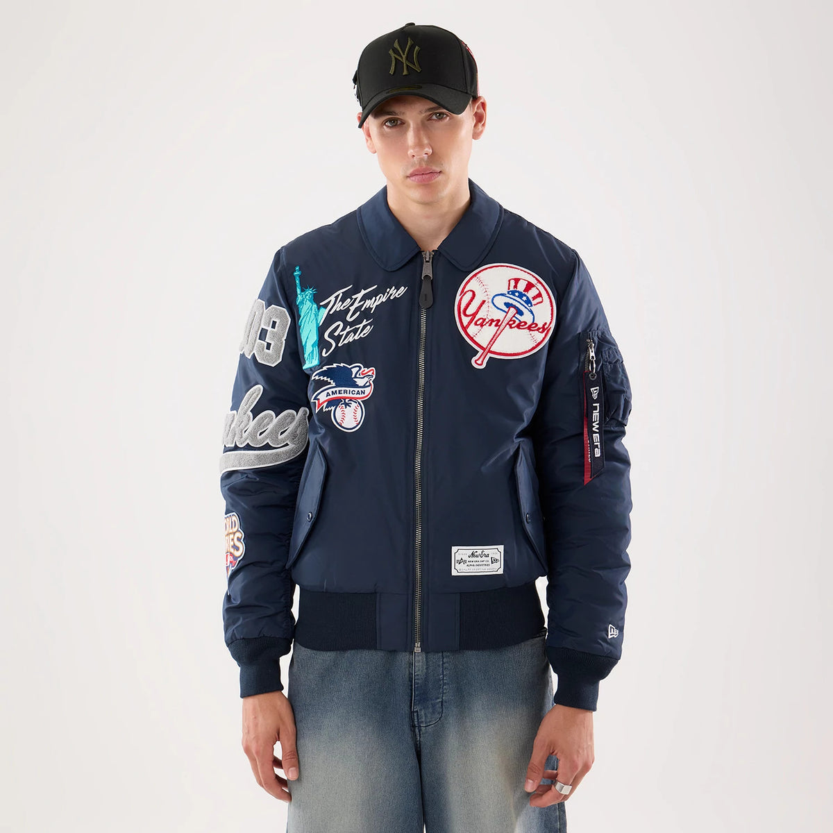 New Era New York Yankees MLB X Alpha Navy Jacket, front view on-model featuring a zip-up closure and various embroidered patches, including a large Yankees logo on the chest and multiple icons of New York, with cuffed sleeves.
