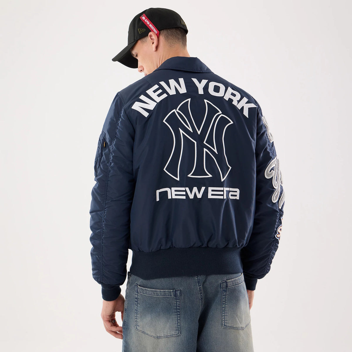 New Era New York Yankees MLB X Alpha Navy Jacket, back view on a model wearing a black cap, showing the large white embroidered Yankees logo under NEW YORK lettering, and new era embroidered near the waistband on the navy back panel.