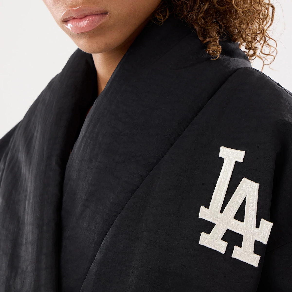 New Era LA Dodgers MLB X Alpha Black Jacket, three-quarter view on a model focusing on the left shoulder, featuring a prominent white embroidered LA Dodgers logo on the black fabric, with a wide collar draped around the neck.