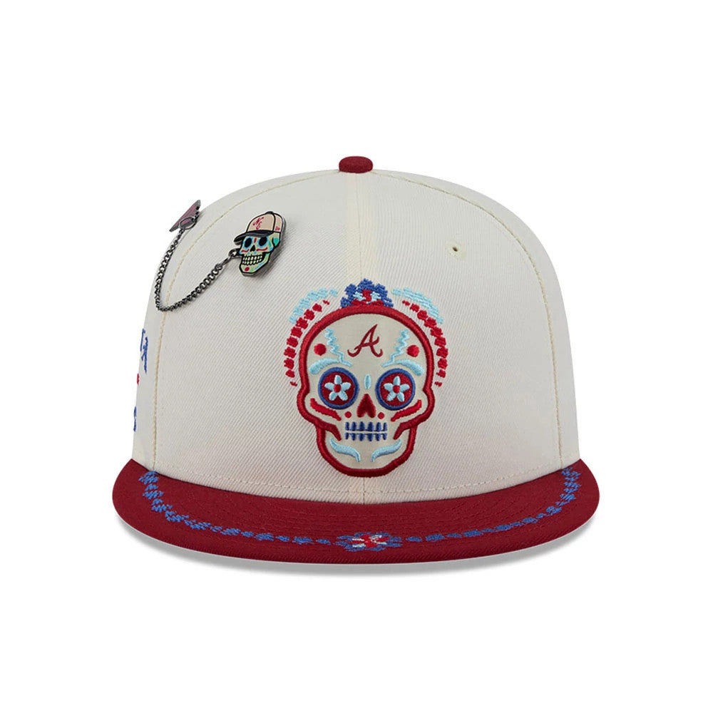 Braves MLB Day Of The Dead Light Beige & Dark Red New Era 59FIFTY Fitted Cap, front view showing an intricately embroidered skull logo in red and blue on the front panel, dark red visor with blue-red floral detail, and hanging skull chain pin.