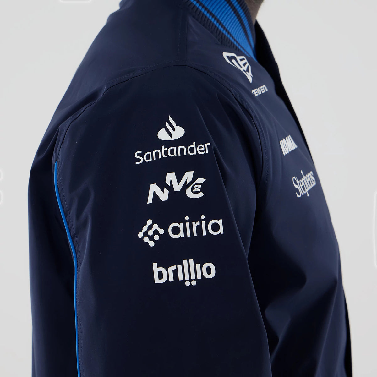 New Era Williams Navy Varsity Jacket, side view showing white logos for Santander, NE, airia, and brllio vertically arranged on the left sleeve, with a New Era embroidered logo on the chest, and a striped blue and black ribbed collar.