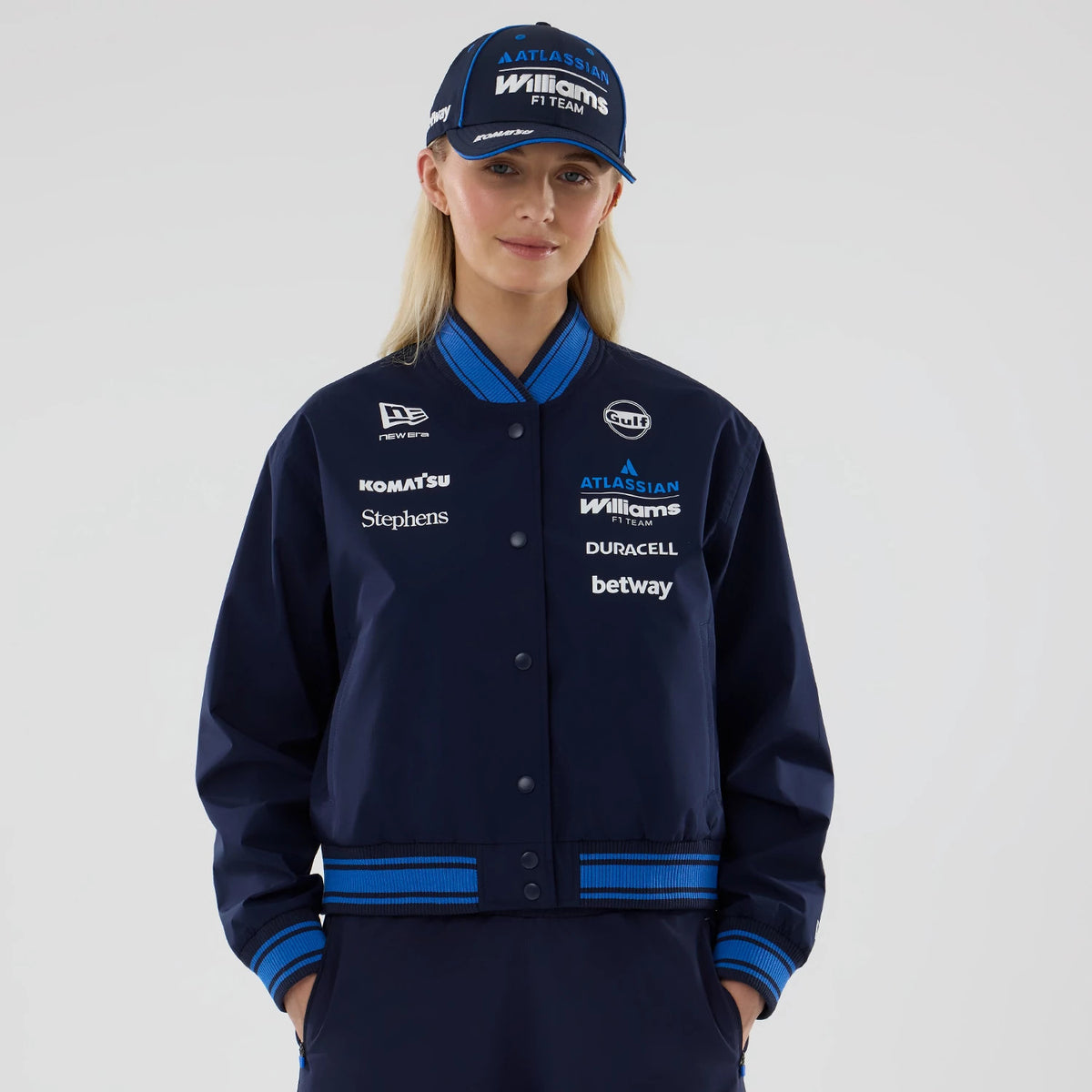 New Era Womens Williams Navy Varsity Jacket, front view on a model, featuring various white sponsor logos including a New Era embroidered logo on the left chest, blue and black ribbed collar, cuffs and hem, and snap button closure down the front.