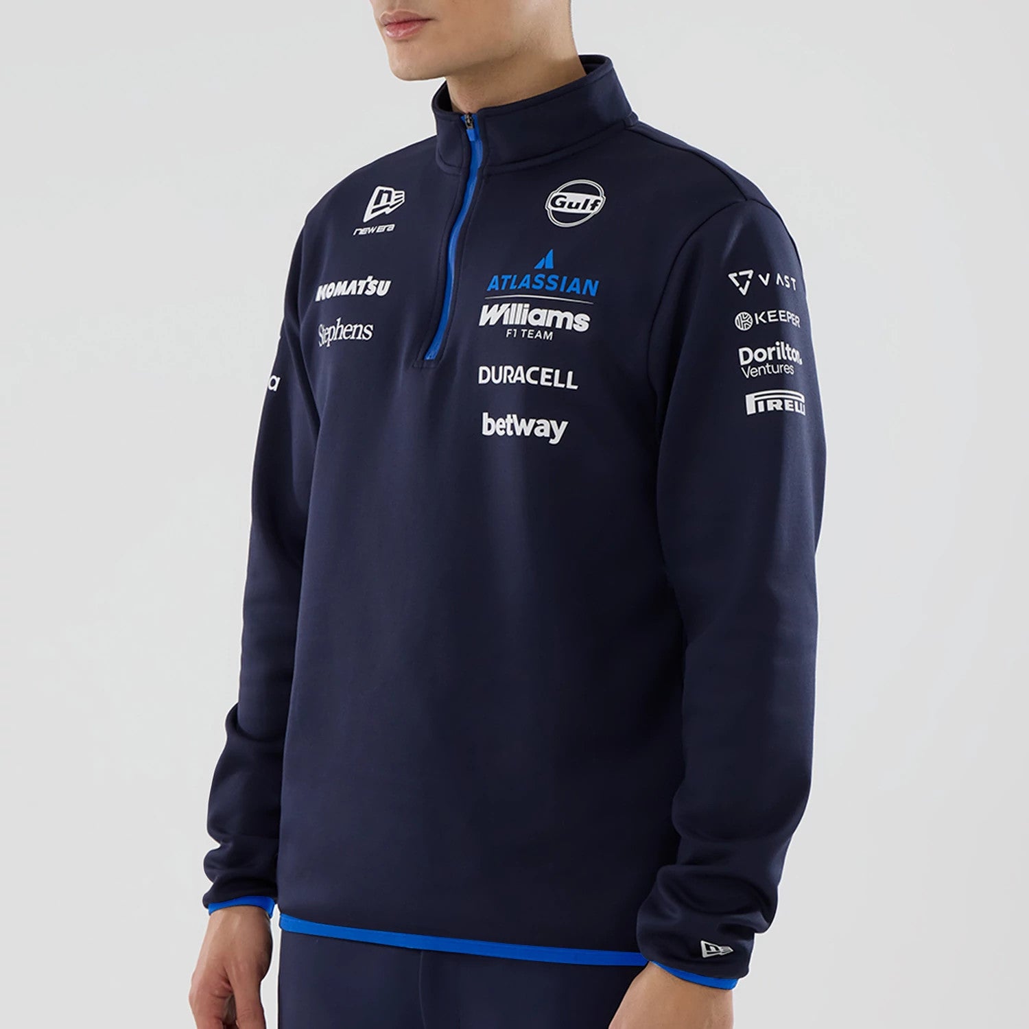 New Era Williams Navy Mid Layer 1/4 Zip Sweater, front three-quarter view on a model displaying multiple sponsor logos in white and blue on the chest and sleeves, with a prominent blue zip and a New Era logo on the left shoulder.