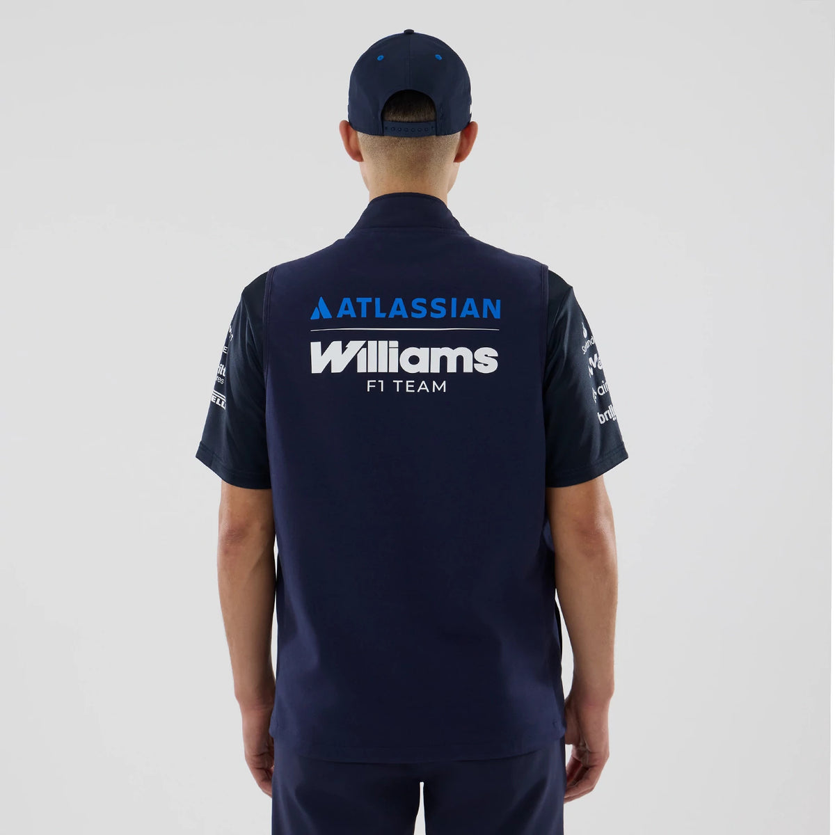 New Era Williams Navy Gilet, back view on a model wearing a matching navy cap, featuring the Atlassian logo in blue above white Williams F1 Team lettering across the upper back, complemented by embroidered sponsor logos on the sleeves.