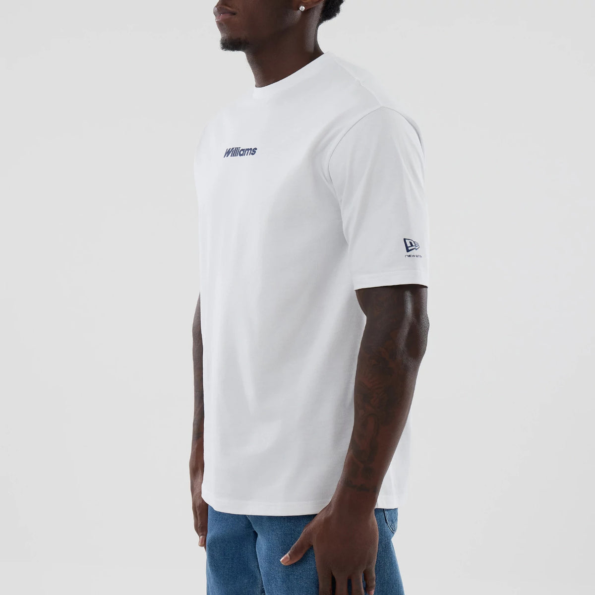 New Era Williams Japan 1996 Script White Oversized T-Shirt, three-quarter view on a model showing the clean white fabric with 'Williams' embroidered in blue script on the chest and the New Era logo embroidered in navy on the left sleeve.