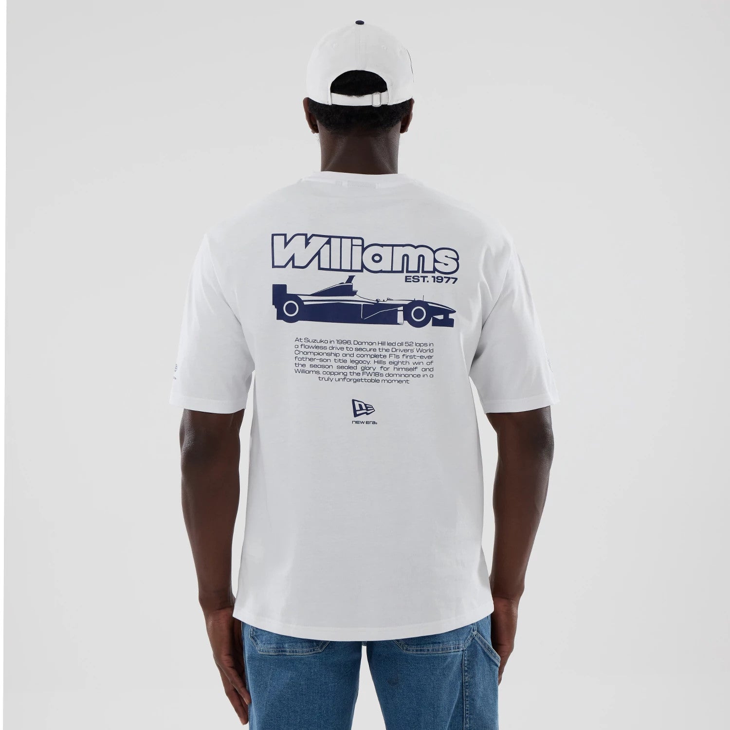 New Era Williams Japan 1996 Script White Oversized T-Shirt, back view on a model with a matching white cap, showcasing a large navy Williams EST. 1977 graphic with a race car illustration and New Era embroidered logo near the lower edge.