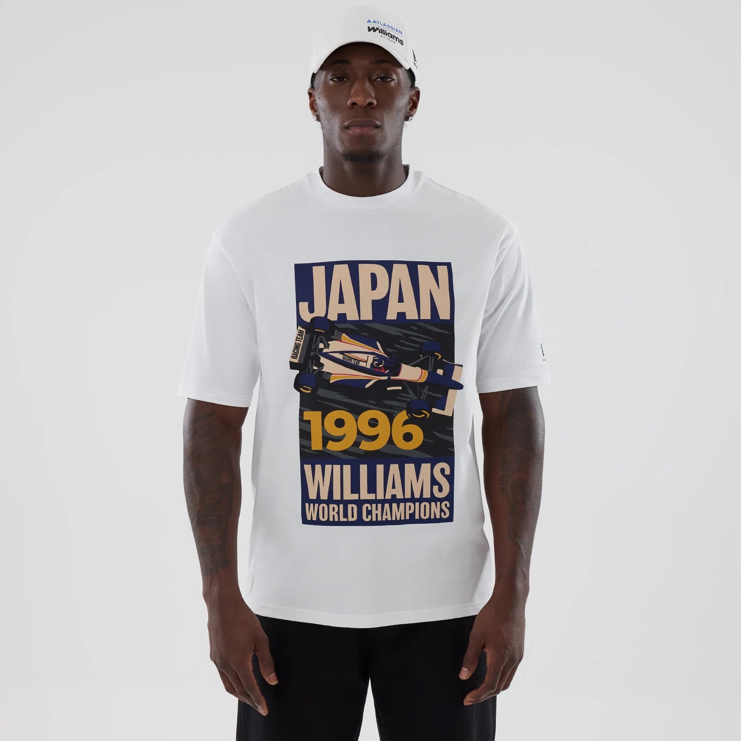 New Era Williams Japan 1996 White Oversized T-Shirt, front view on a model styled with a white cap, displaying a printed graphic of a race car with JAPAN 1996 WILLIAMS WORLD CHAMPIONS lettering prominently across the chest.