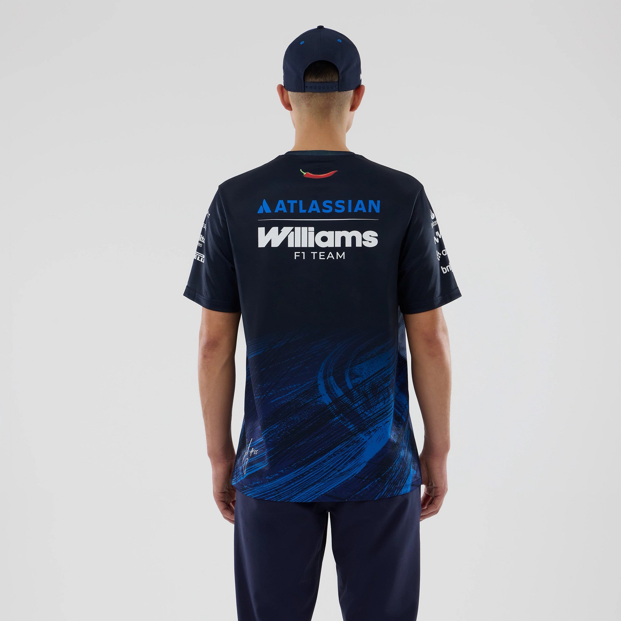 New Era Williams Carlos Sainz Navy Tech T-shirt, back view on a model with a navy cap, showing the Williams F1 Team branding in white across the upper back, Atlassian logo in blue above, and dynamic blue graphics on the lower half.