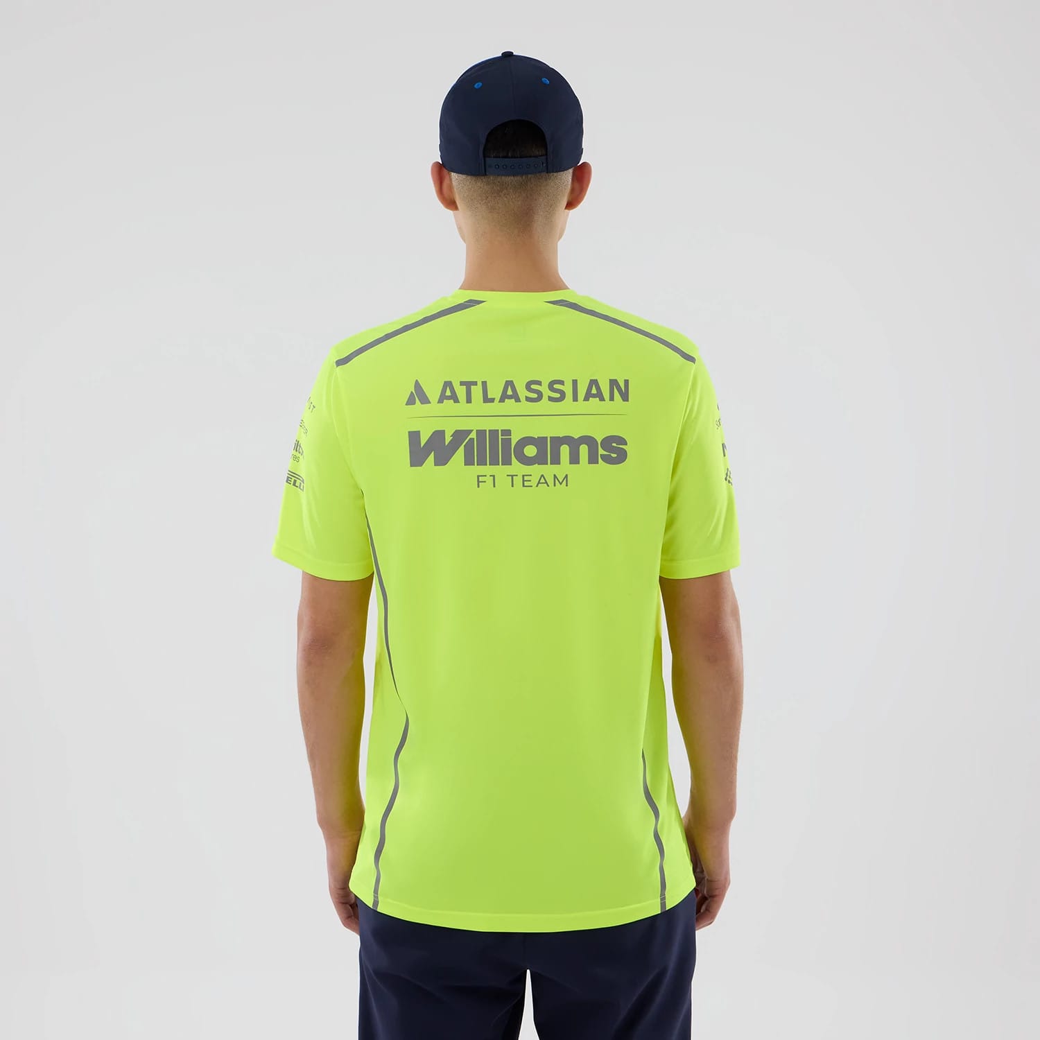 New Era Williams Set Up Yellow T-Shirt, back view on-model showing Atlassian and Williams F1 Team printed lettering in grey across the upper back, grey stripe along the sleeves, paired with a dark cap and shorts.