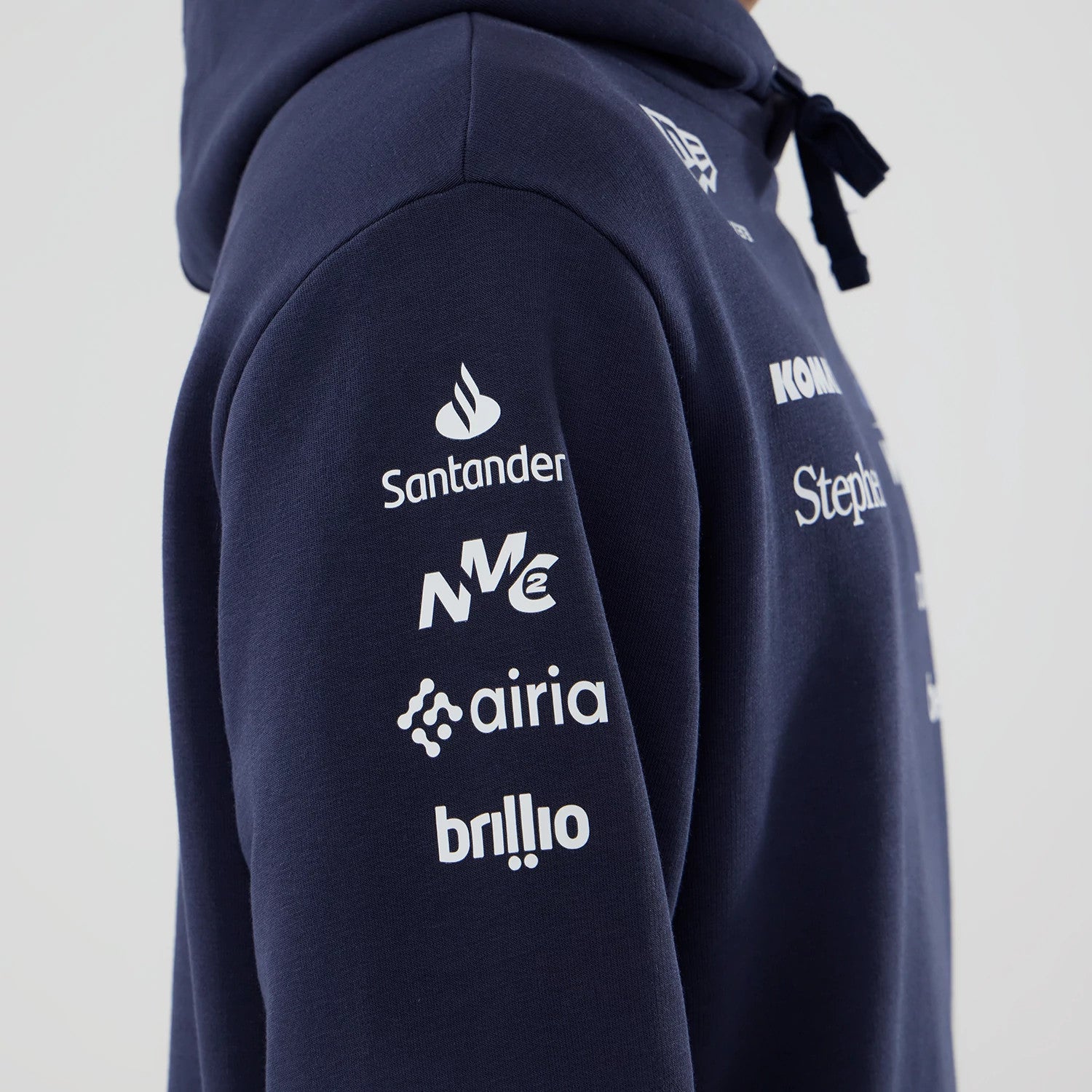 New Era Williams Replica Navy Pullover Hoodie, side view showing multiple white sponsor logos printed vertically down the sleeve, a New Era logo embroidered near the shoulder, and a drawn hood cord dangling at the front.