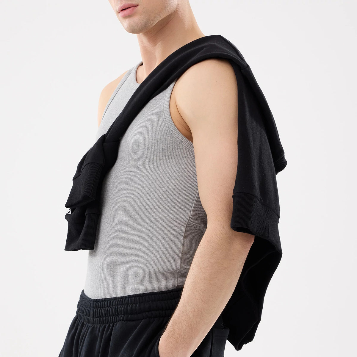 New Era LA Dodgers MLB Rib Grey Vest, side view on a model with a casual styling, showing the ribbed texture of the grey vest, scoop neckline, and the armhole design, paired with black trousers and a black sweatshirt draped over the shoulder.