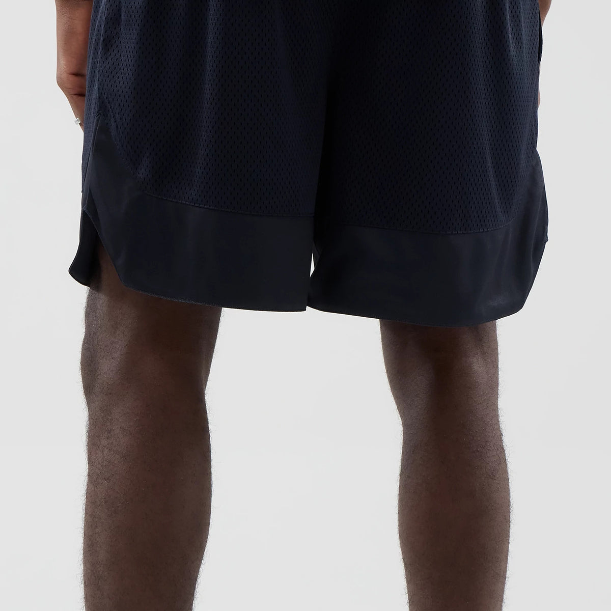 New Era Mesh Navy Oversized Shorts, back view showing the shorts worn on a model with a mesh texture throughout, a solid band along the bottom hem, and a loose fit designed for casual comfort and style.