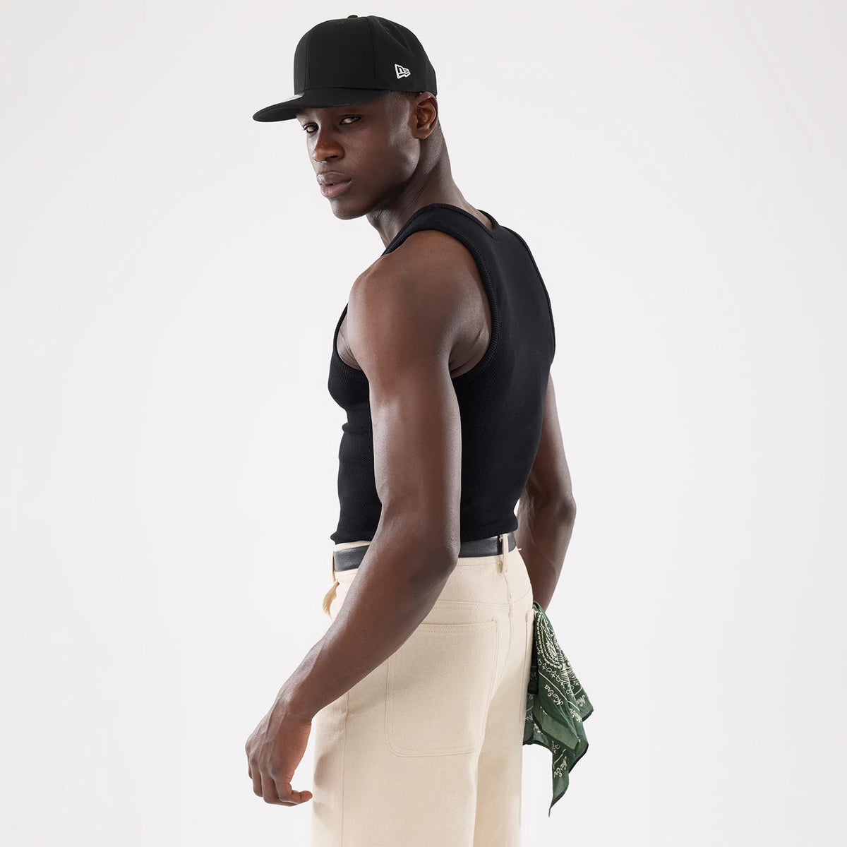New Era Rib Black Vest, back view on a model styled with a black cap and beige trousers, highlighting the ribbed texture of the vest and the fitted silhouette, complemented by a green bandana in the back pocket.