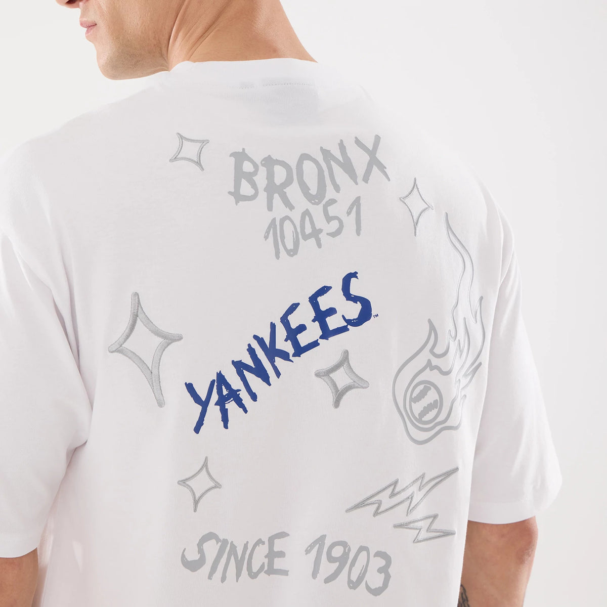New Era New York Yankees MLB 59FIFTY Day Graphic White T-Shirt, back view on-model showing grey Bronx 10451 text and silver star graphics, blue Yankees lettering in the centre, complemented by Since 1903 script at the base near the hem.