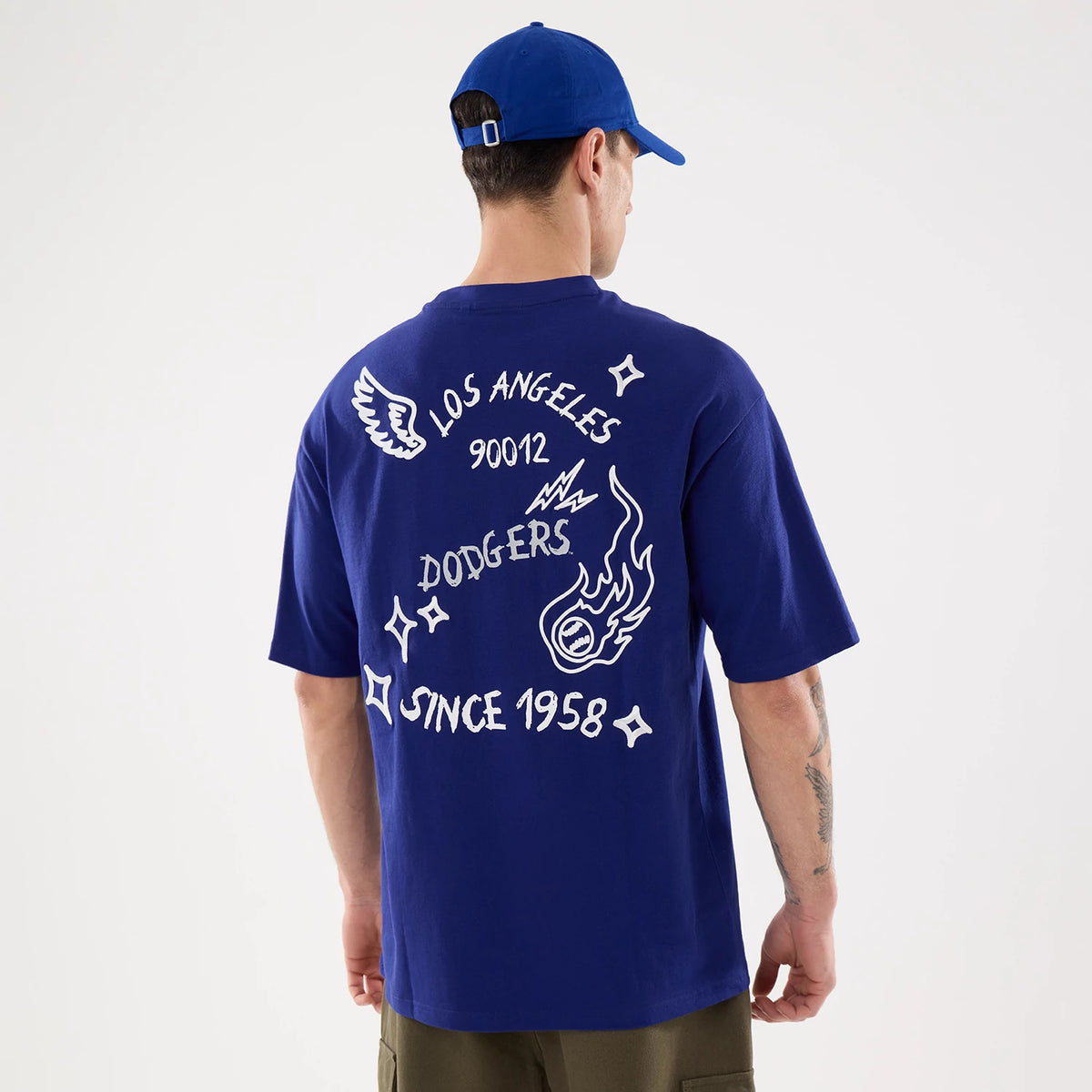 New Era LA Dodgers MLB 59FIFTY Day Graphic Dark Blue T-Shirt, back view on-model showcasing white printed graphics including 'Los Angeles 90012', 'Dodgers', and 'Since 1958' across the shoulders, with a flame.