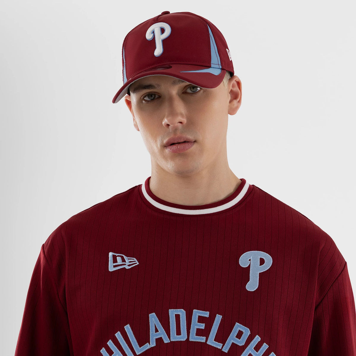 New Era Philadelphia Phillies MLB Dark Red Oversized T-Shirt, front view on a model with matching cap, showing the light blue embroidered P logo on the upper left chest, white New Era logo on the right.