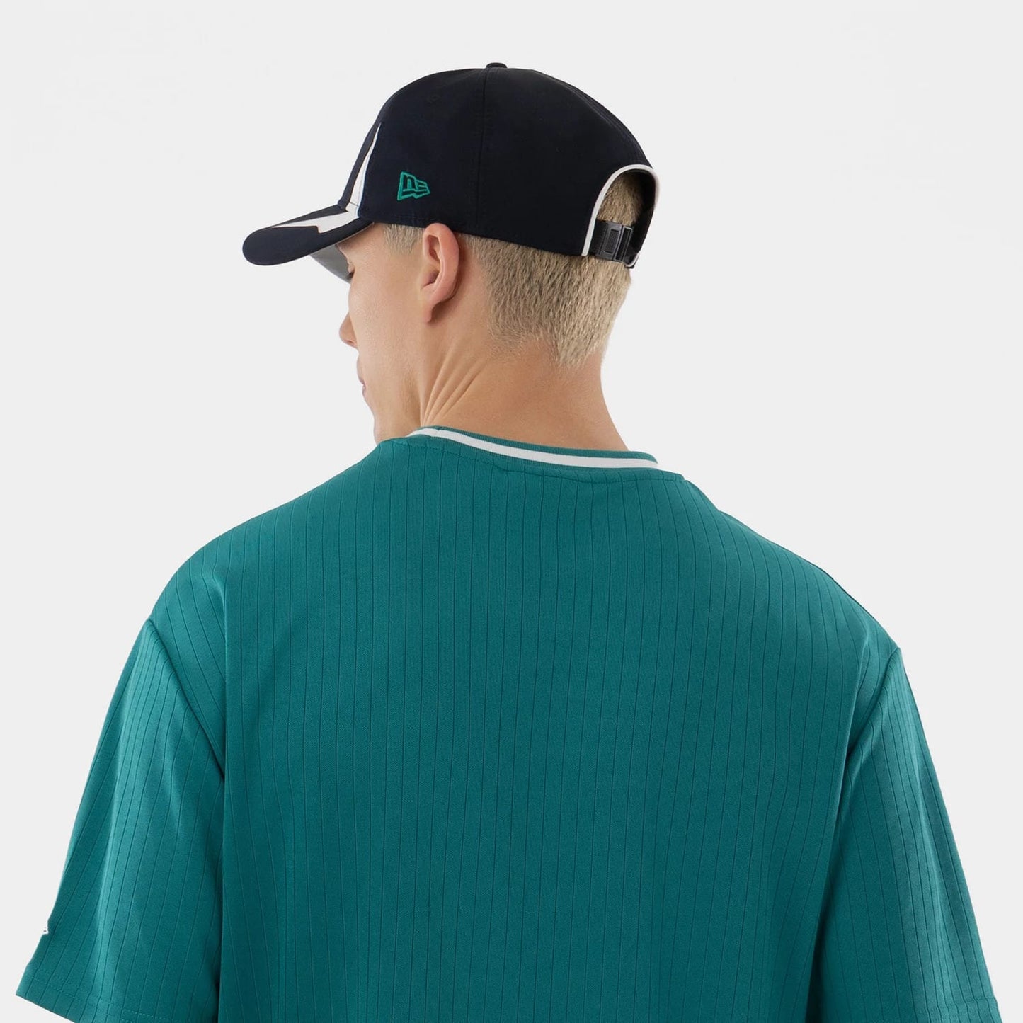New Era Seattle Mariners MLB Green Oversized T-Shirt, back view on a model seen wearing a black cap, displaying a plain green shirt with vertical stripes and a contrasting neckline, creating a classic baseball look.