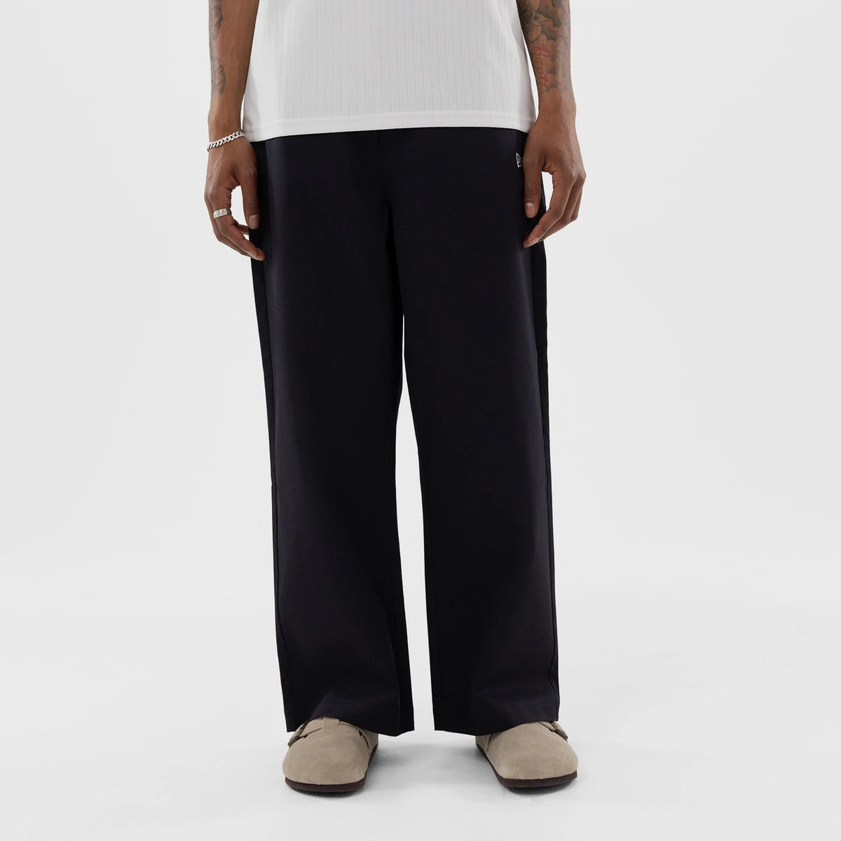 New Era LA Dodgers MLB Navy Woven Chinos, front view on a model showing full-length navy trousers with a wide-leg fit, pleat down the front, and the New Era flag logo embroidered near the left pocket.