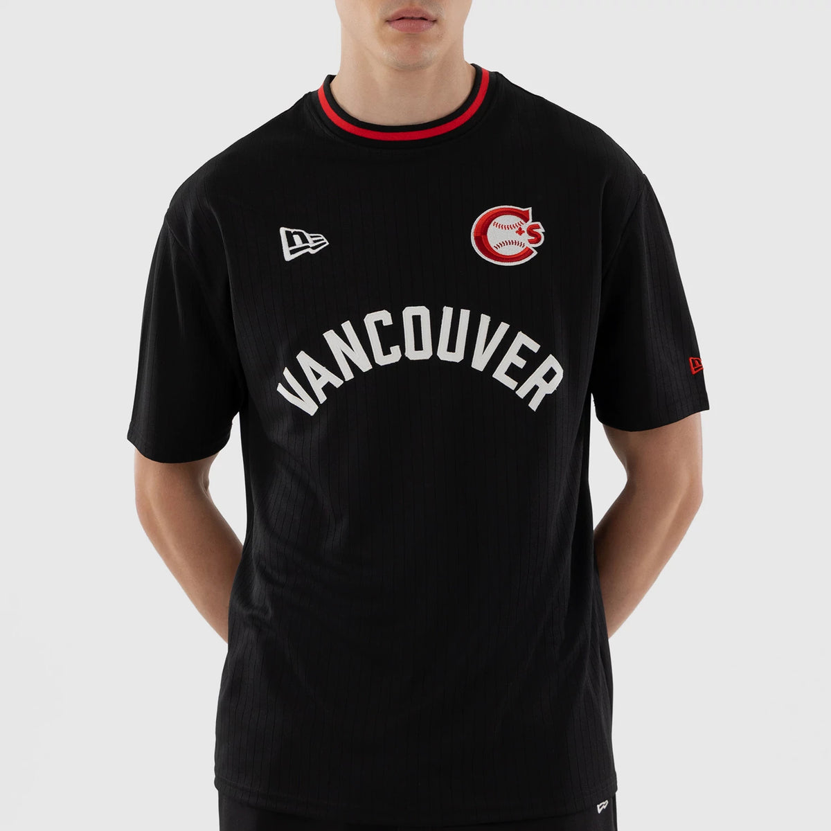 New Era Vancouver Canadians MiLB Black Oversized T-Shirt, front view on a model showing a white Vancouver arched logo across the chest, a red and white embroidered team logo on the right side, and an embroidered New Era flag on the left shoulder.