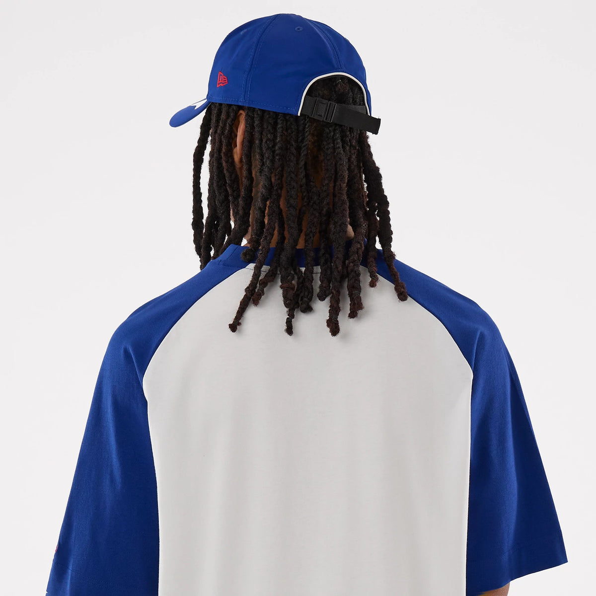 New Era LA Dodgers MLB White Boxy T-Shirt, back view on-model with a blue cap, showing blue sleeves and upper back with a curved white panel, and the cap featuring an embroidered red New Era logo on the side.