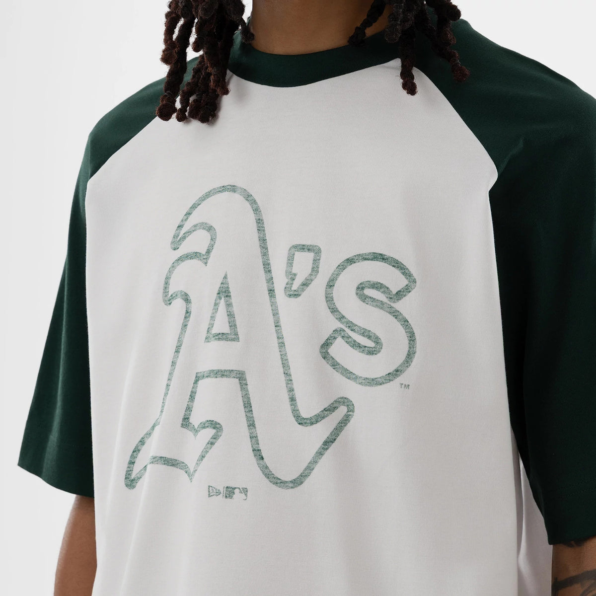 New Era Athletics MLB White Boxy T-Shirt, front view on a model showing a large green printed A's logo in the centre of the white body, with contrasting dark green raglan sleeves and collar framing the graphic.