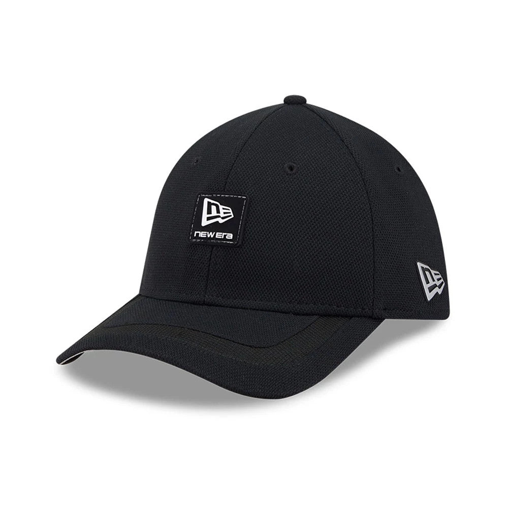 New Era Golf Rubber Patch Black 39THIRTY M-Crown Stretch Fit Cap, three-quarter view showing a black patch with a white New Era logo on the front panel, a curved black visor, and a grey embroidered New Era flag logo on the left side.