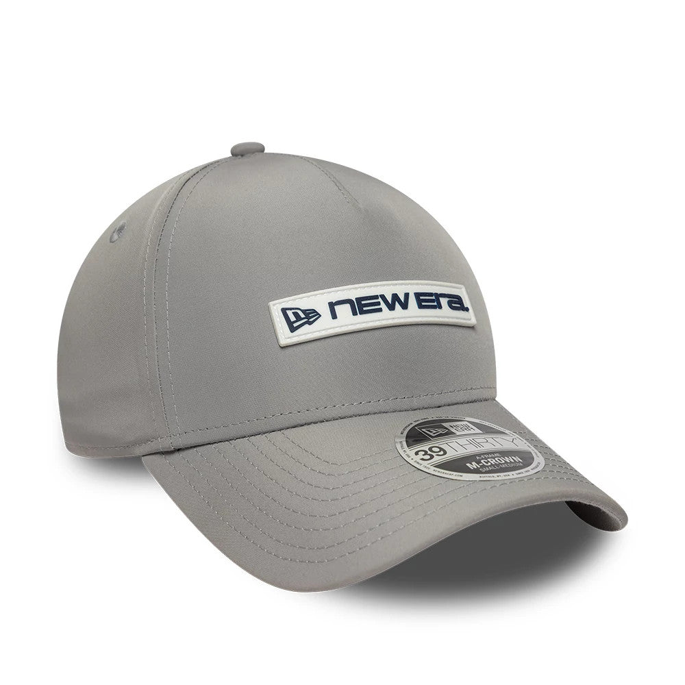 New Era Rubber Patch Grey New Era 39THIRTY M-Crown A-Frame Stretch Fit Cap, three-quarter view showing the raised New Era logo on the front panel in navy and white, pre-curved grey visor, and grey 39THIRTY size sticker.