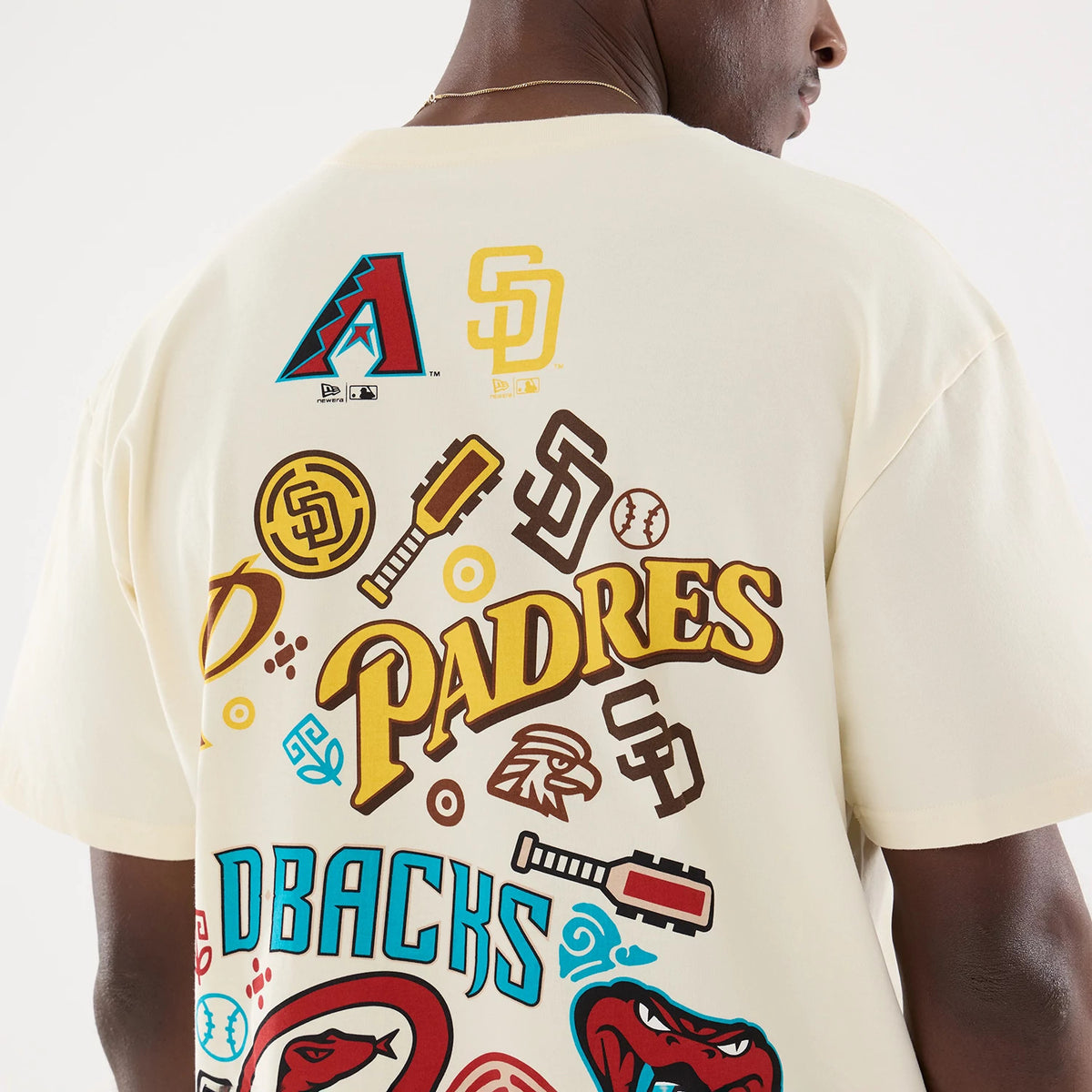 New Era Dueling Logo MLB Mexico City Series 2026 Script Cream T-Shirt, back view on a model highlighting graphics with Padres lettering prominently displayed, various MLB team logos including a red baseball bat, and a cream-coloured fabric.