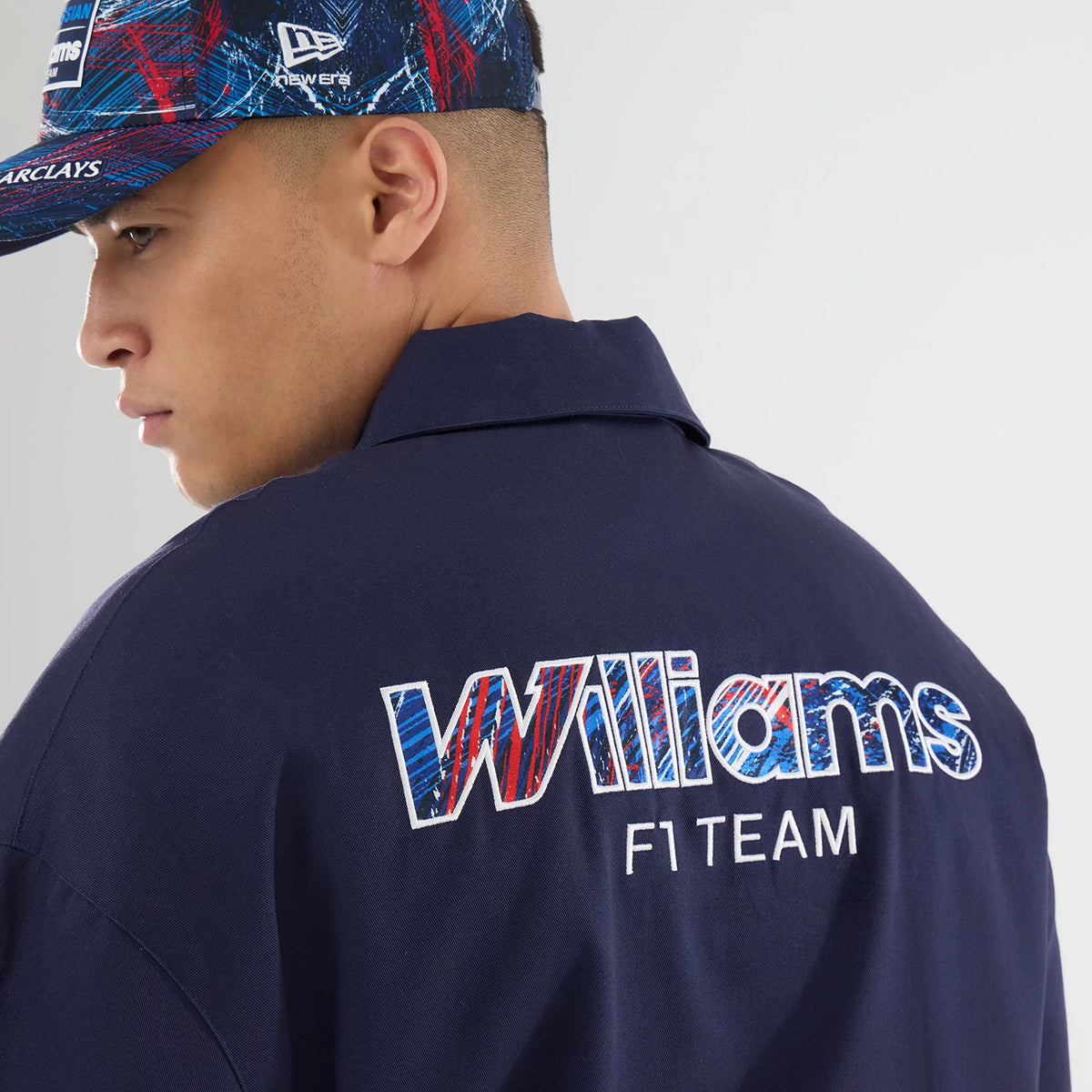 New Era Williams GB Race Special Navy Collared Jacket, back view showing a model wearing it with a matching cap, featuring a large embroidered Williams F1 Team logo in red, blue, and white on the upper back beneath the collar.
