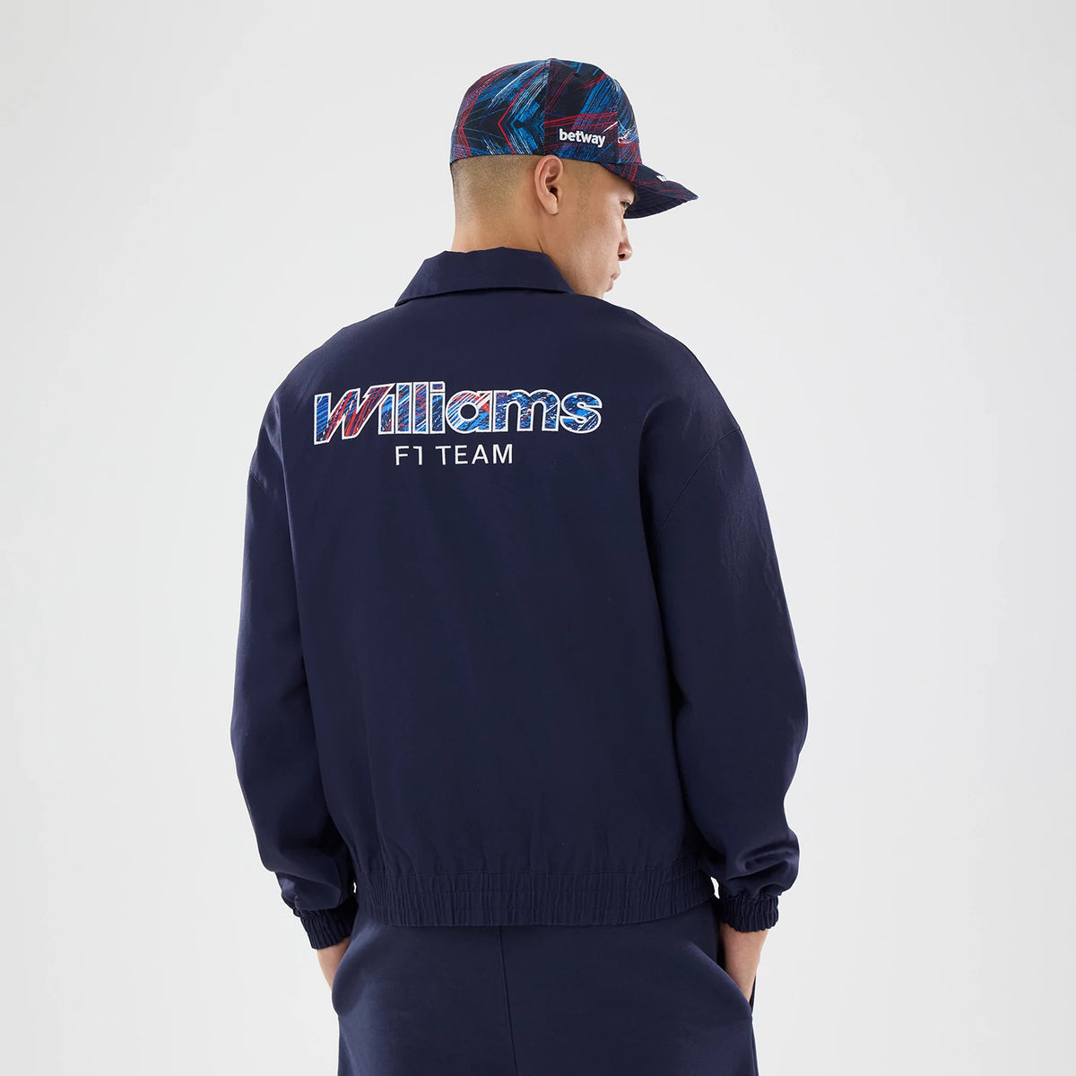 New Era Williams GB Race Special Navy Collared Jacket, back view on-model showcasing the embroidered Williams F1 Team logo in red, white, and blue lettering on the upper back, with the relaxed-fit navy jacket styled casually.