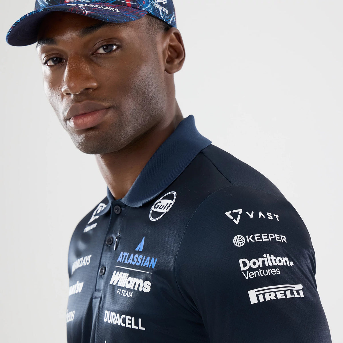 New Era Williams GB Race Special Navy Tech Polo T-Shirt, front view on a model with a colourful cap, featuring multiple white printed logos across the chest including the Williams F1 Team, and additional sponsor logos on the sleeves.