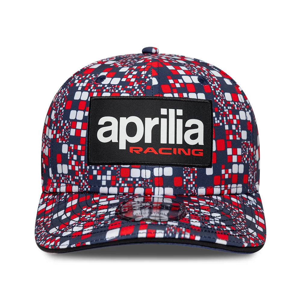Aprilia Replica Silverstone Race Special Blue New Era 9SEVENTY Stretch Snap Adjustable Cap, front view showing a large black and white Aprilia Racing patch logo on the front panel, red and blue geometric pattern.