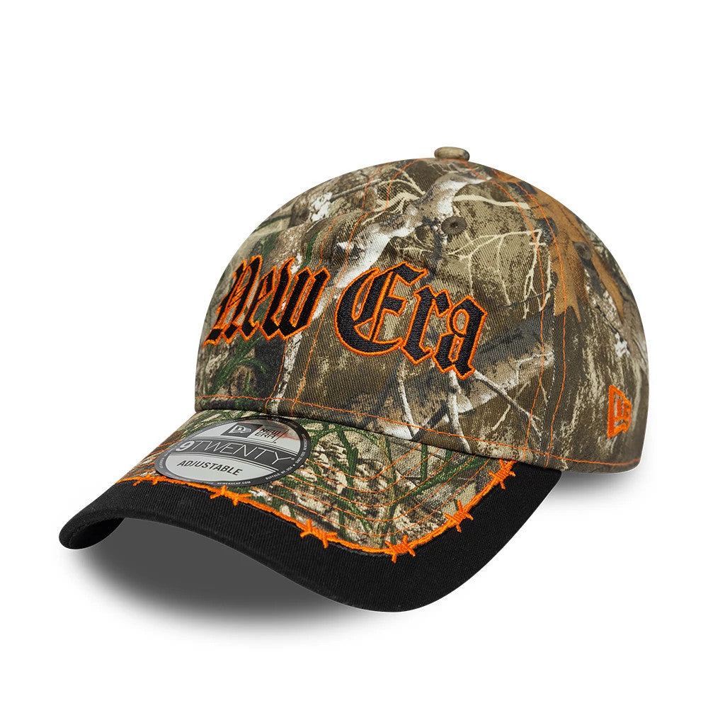 New Era Real Tree Assorted Print New Era 9TWENTY Adjustable Cap, three-quarter view showing orange embroidered New Era lettering on the camo front panel, a contrasting black visor with orange stitch details, and a 9TWENTY size sticker.