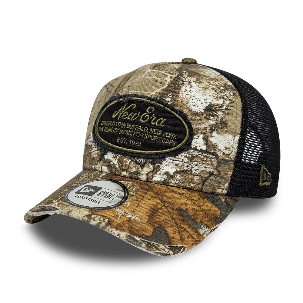 New Era Heritage Patch Realtree Camo New Era 9FORTY A-Frame Trucker Adjustable Cap, three-quarter view showing an oval heritage patch with gold embroidery, a curved Realtree camo visor with a New Era adjustable sticker, and black mesh rear panels.