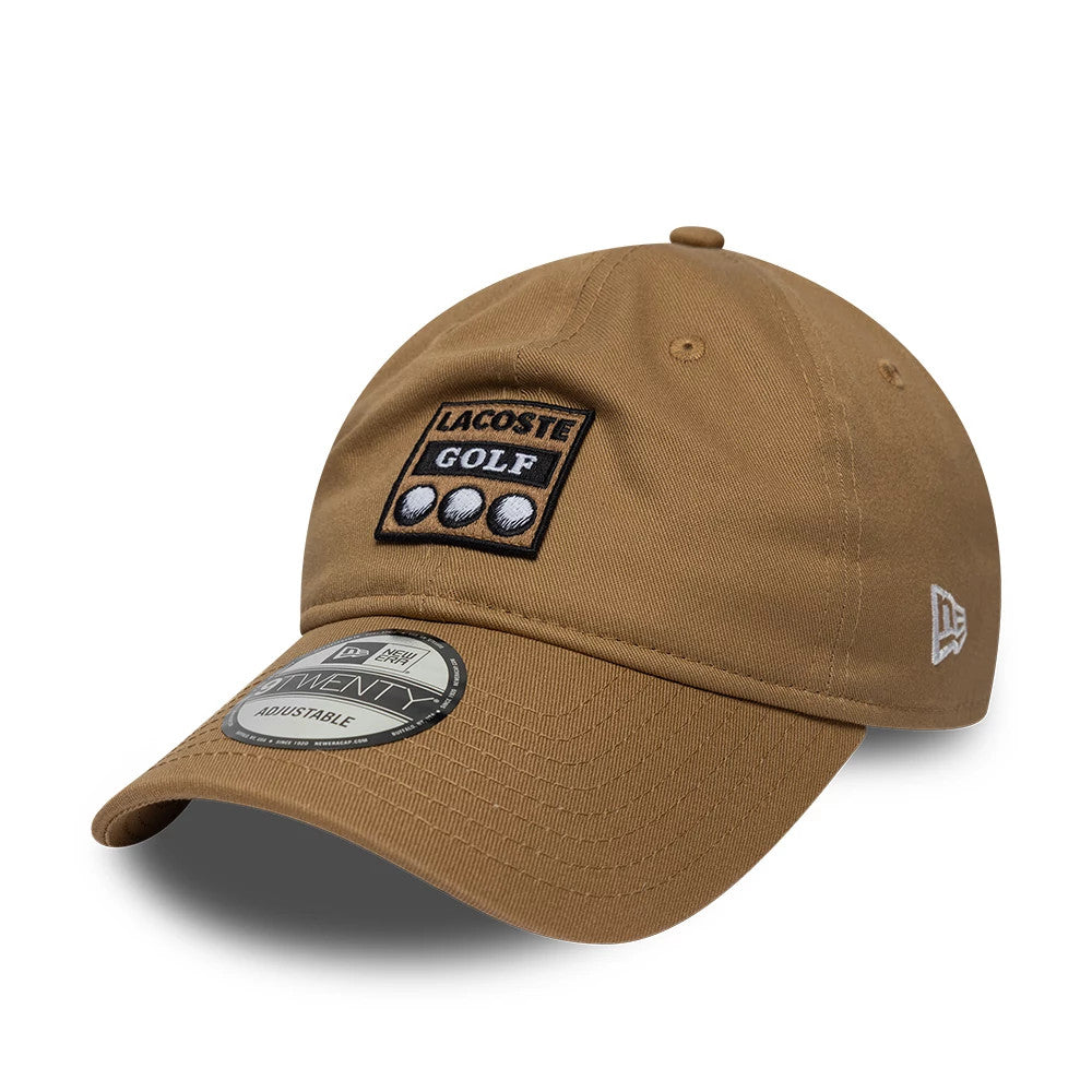 Lacoste X New Era Beige 9TWENTY Adjustable Cap, three-quarter view showing a black and white embroidered Lacoste Golf logo with three golf balls on the front panel, a New Era flag logo on the left side, and a 9TWENTY size sticker on the curved visor.