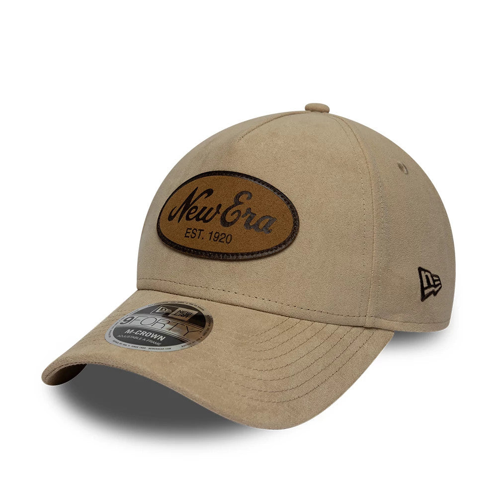 New Era Faux Suede Light Beige 9FORTY M-Crown A-Frame Adjustable Cap, three-quarter view showing a brown oval New Era Est. 1920 patch on the front panel, black New Era flag logo on the left side, and 9FORTY size sticker on the curved visor.