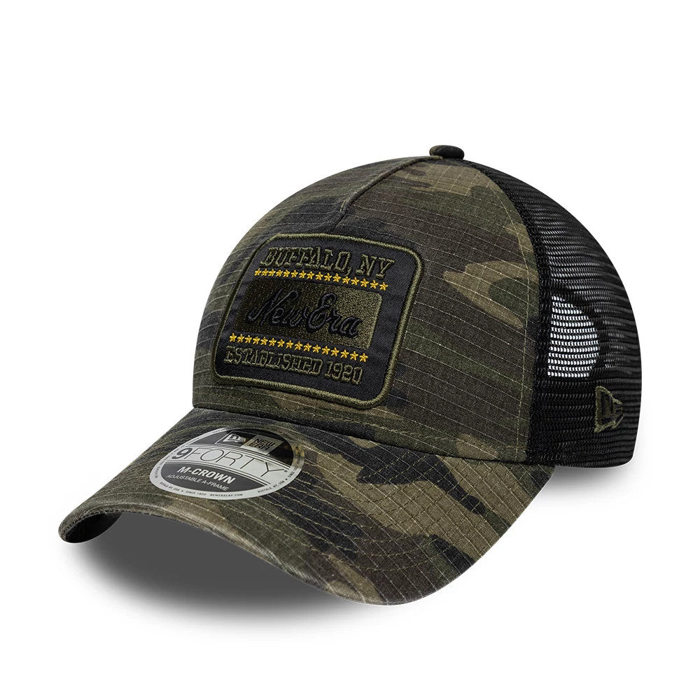 New Era Camo Woodland Camo 9FORTY M-Crown A-Frame Trucker Adjustable Cap, three-quarter view showing a large rectangular embroidered patch on the structured camo crown, black New Era flag logo on the side mesh.