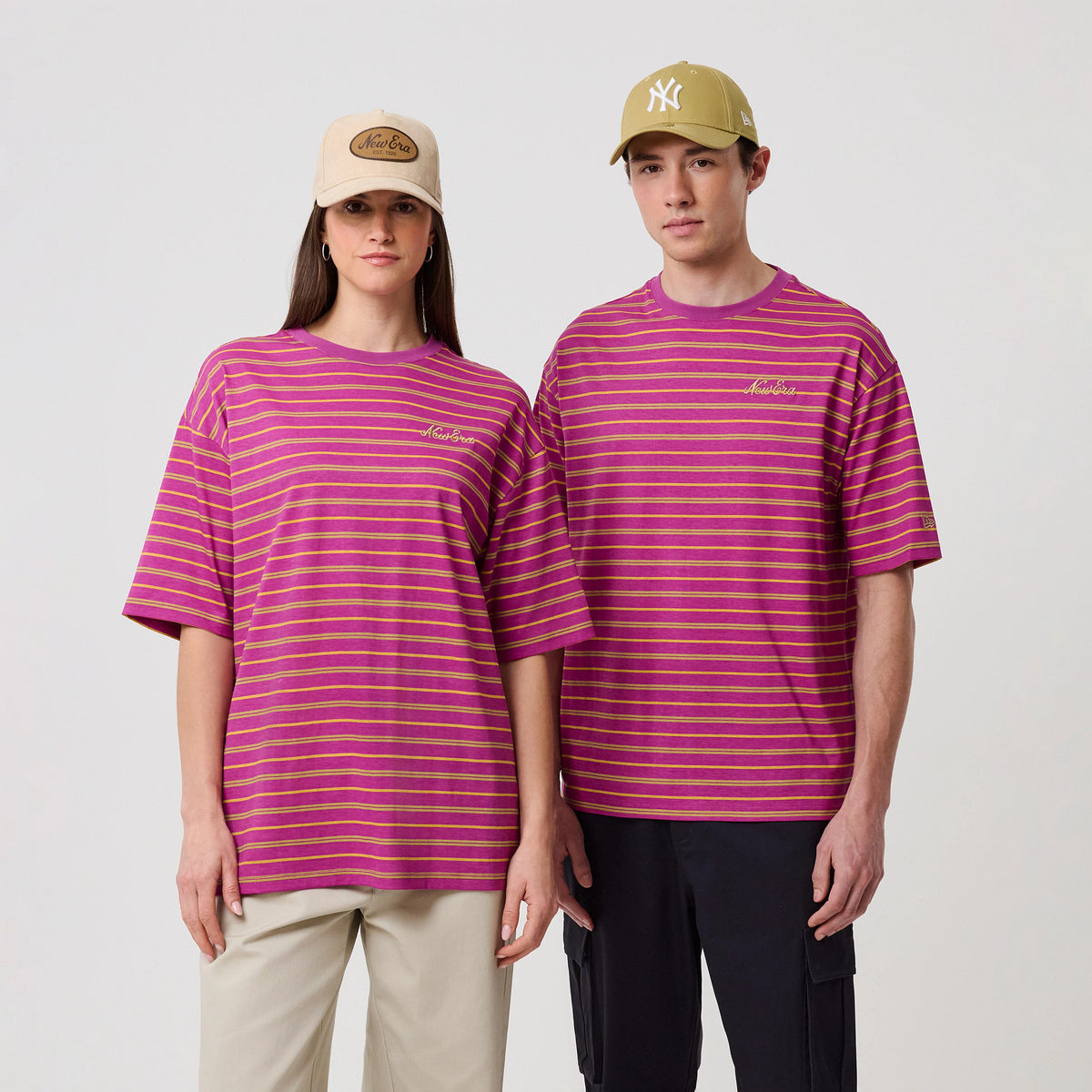 New Era Stripe Bright Purple T-Shirt, front view on models showing pink and yellow striped design, an embroidered New Era logo on the left chest, and short sleeves, with a casual fit styled with beige and khaki caps.