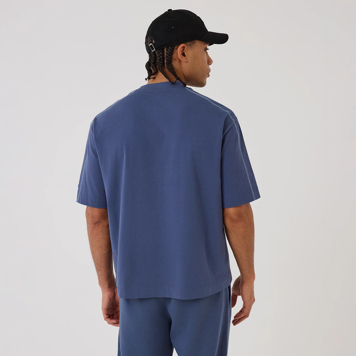 New Era LA Lakers NBA Graphic Dark Blue Boxy T-Shirt, back view on a model wearing matching dark blue shorts and a black cap, showing the plain back of the boxy tee with a relaxed fit and short sleeves.