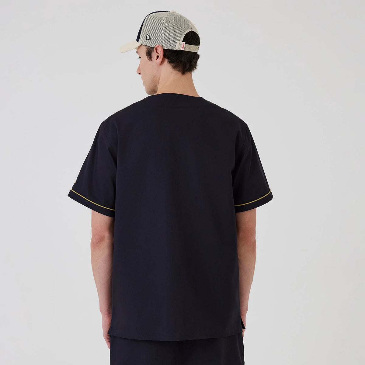 New Era Navy Straight Hem Jersey, back view on a model wearing a mesh cap, showing the plain navy back with yellow piping along the short sleeves and a straight hem for a clean and simple style.