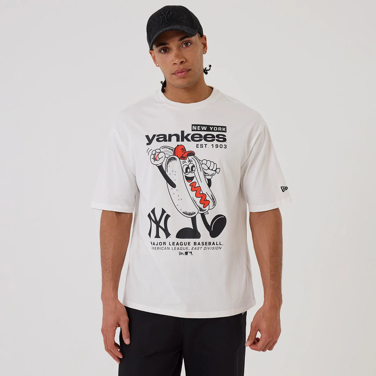 New Era New York Yankees MLB Hotdog Graphic White Oversized T-Shirt, front view on a model showing a playful hotdog character graphic in black and red, with Yankees text above and the New York Yankees logo printed below on the white fabric.