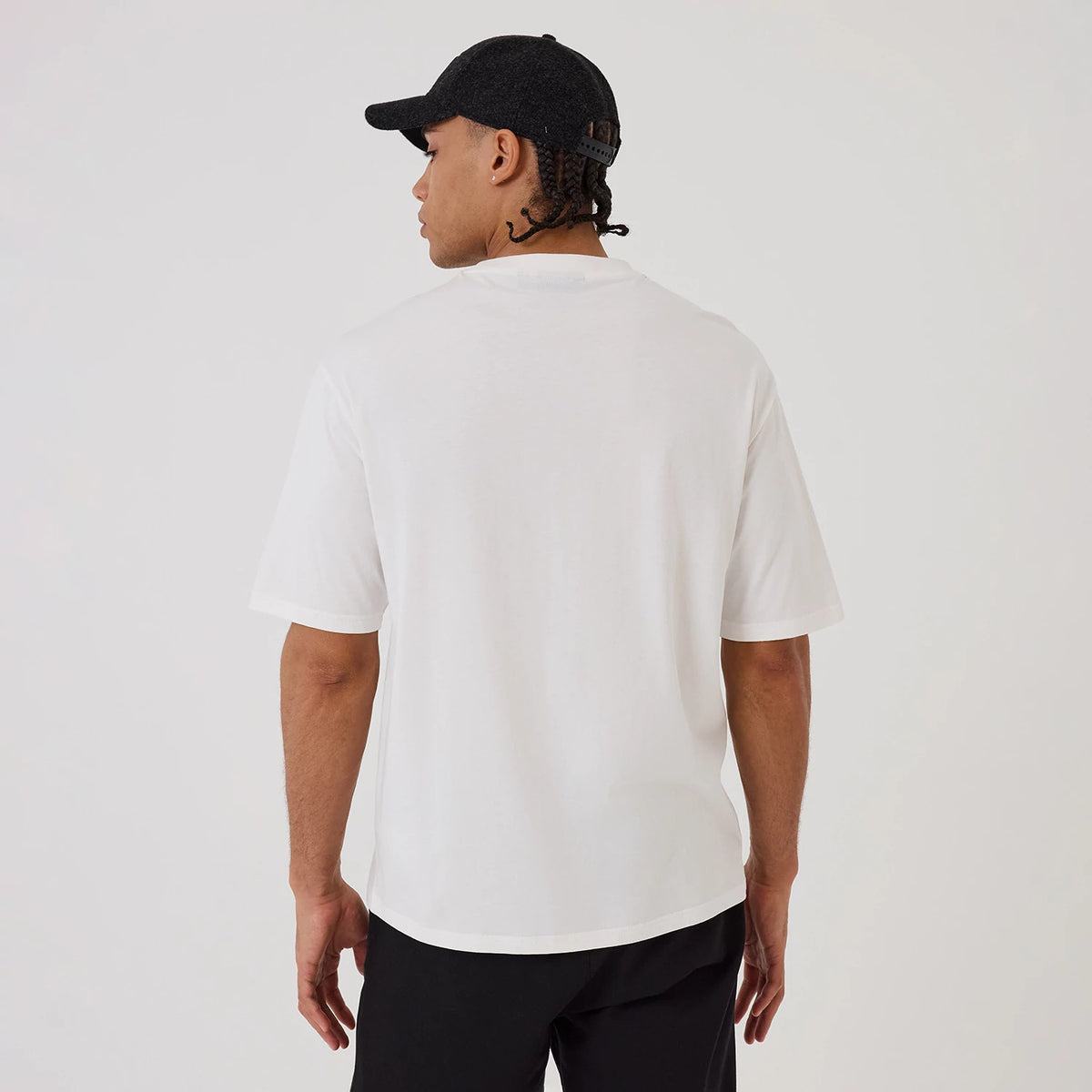 New Era New York Yankees MLB Hotdog Graphic White Oversized T-Shirt, back view on a model wearing black trousers and a cap, showing the plain white back with a relaxed fit and short sleeves extending to the elbow.