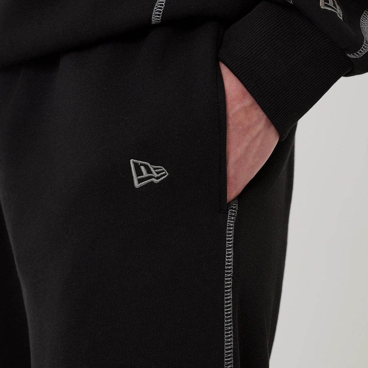 New Era Chicago Bulls NBA Graphic Black Straight Leg Joggers, close-up view showing the embroidered New Era flag logo on the right leg, with grey stitching along the seams and a hand in the side pocket.