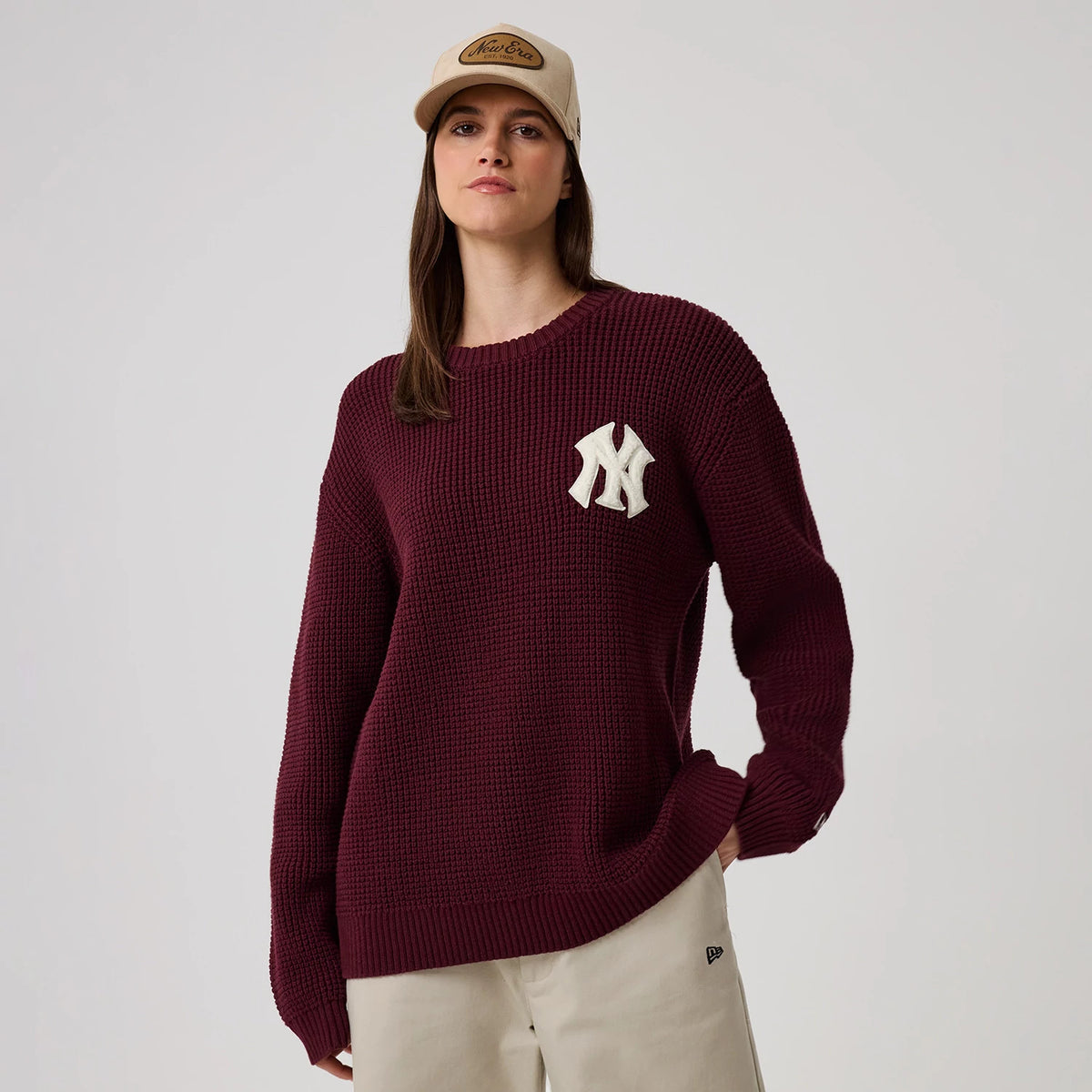 New Era New York Yankees MLB Waffle Knit Dark Purple Crew Neck Sweater, front view on a model showcasing the prominent white NY logo on the chest, textured knit pattern, and ribbed cuffs, paired with beige trousers featuring the New Era flag logo.