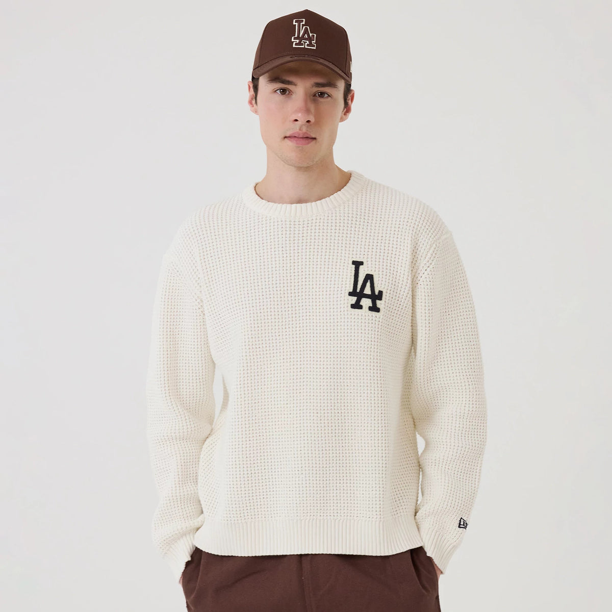 New Era LA Dodgers MLB Waffle Knit Open White Crew Neck Sweater, front view on a model with a brown LA cap, featuring the LA logo embroidered in black on the left chest, and a New Era flag logo on the left sleeve cuff.