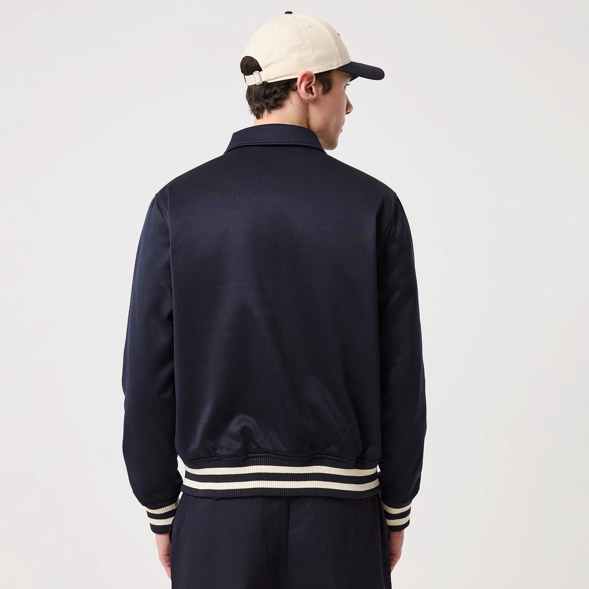 New Era New York Yankees MLB Navy Collared Jacket, back view on-model showcasing the solid navy design with a crisp collar, contrasting white and navy striped ribbed hem and cuffs, and styled with a cream and black cap, creating a coordinated look.